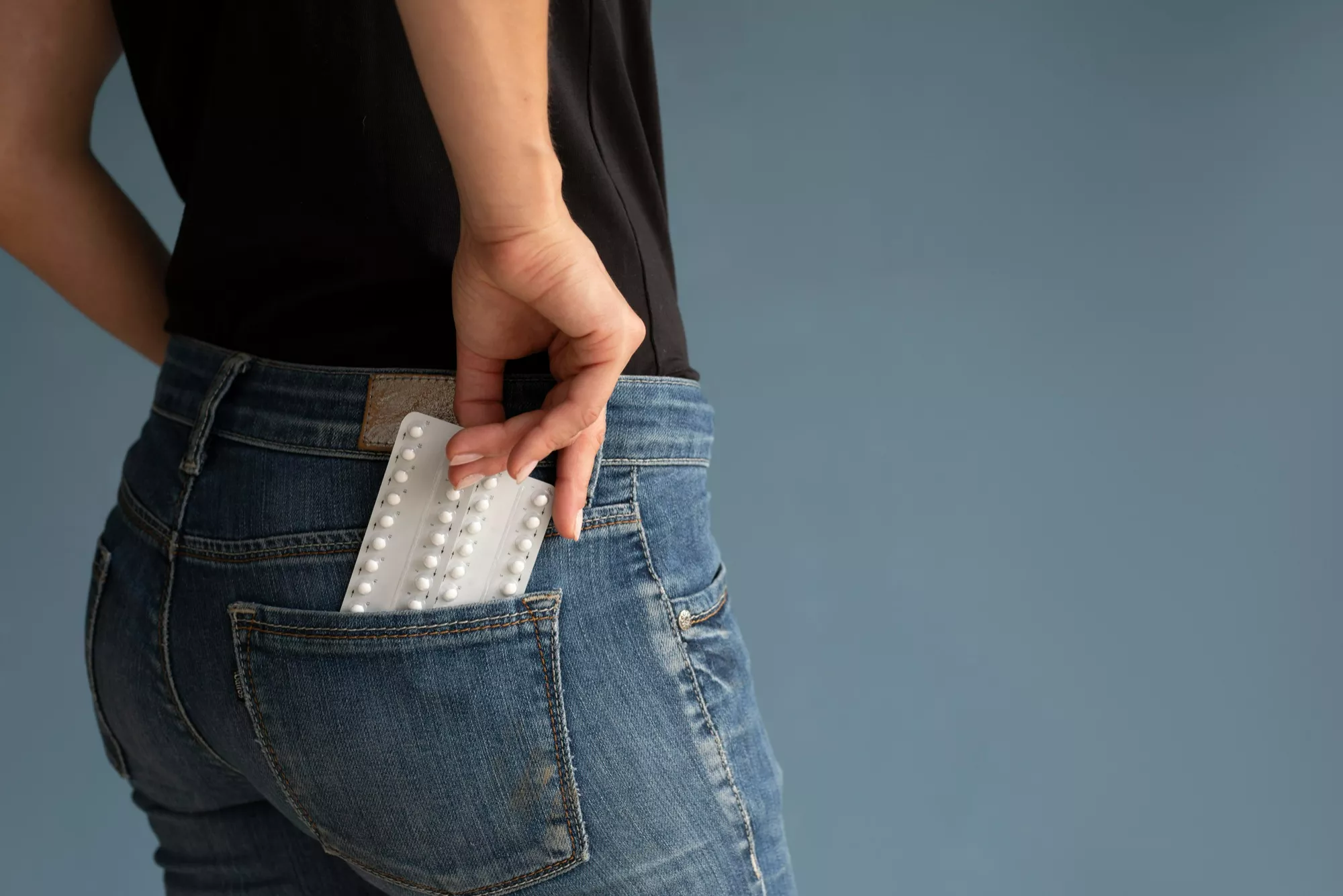femme range une plaquette de pilule dans la poche arrière de son jean