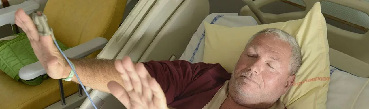 un patient alité ferme les yeux et lève ses bras