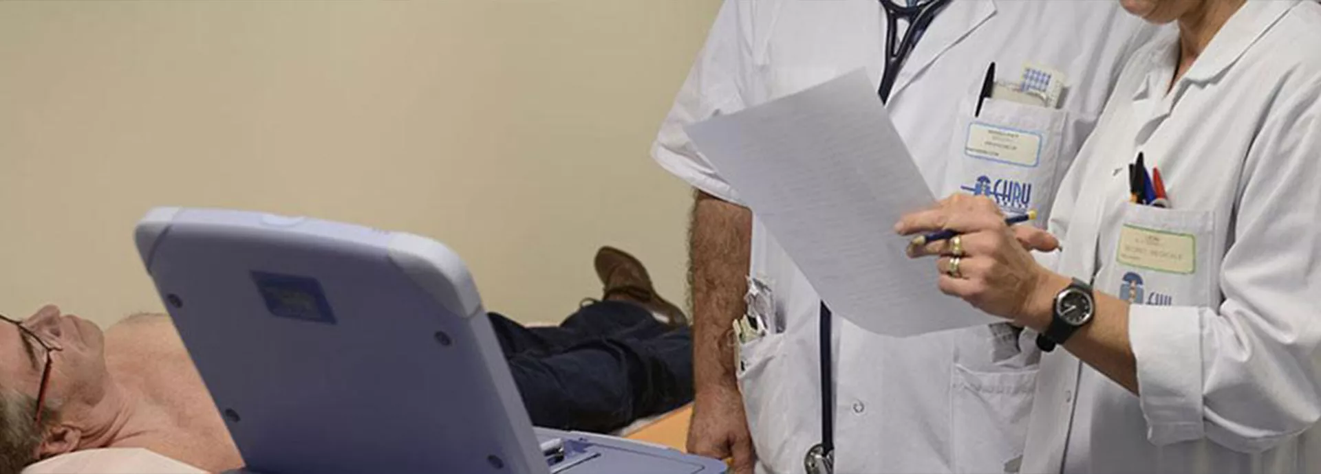deux soignants regardent les résultats d'examens, le patient est allongé sur un lit médicalisé