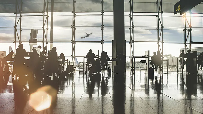 dans un terminal d'aéroport des gens attendent leur vol, on voit un avion en arrière-plan décoller