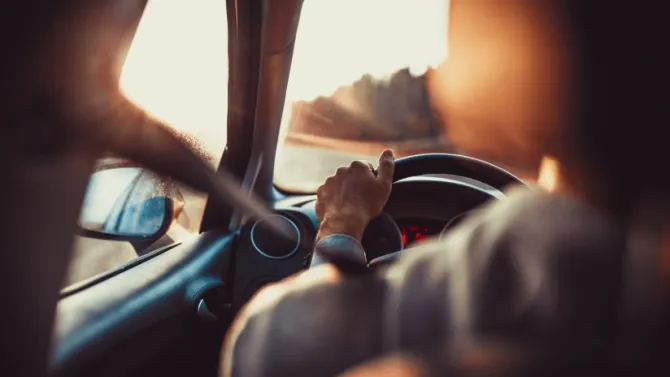 Un homme au volant d'une voiture, la main sur le volant, le regard tourné vers la route devant lui