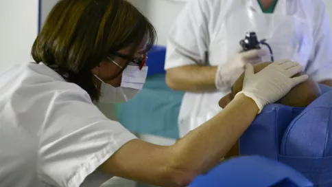 une médecin en blouse blanche et masque pose la main sur un patient pour un soin