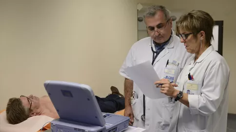 deux soignants regardent les résultats d'examens, le patient est allongé sur un lit médicalisé