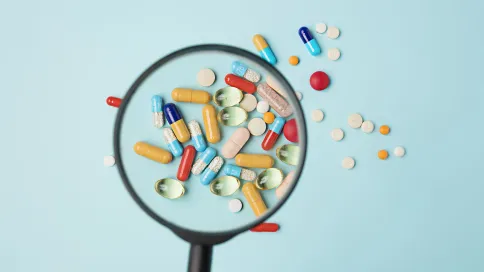 Comprimés, pilules et gélules pharmaceutiques placés sous une loupe, sur un fond bleu pastel